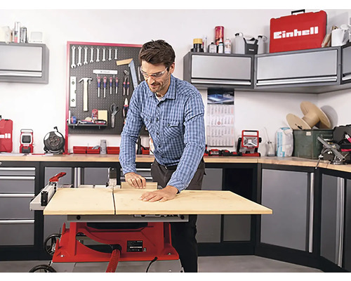 Muž pracuje s stolní pilou v dílně s nářadím a skříněmi.