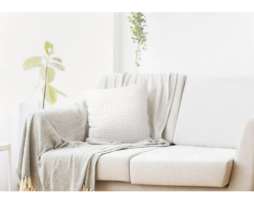 Světlý obývací pokoj s pohovkou, polštářem a přehozem