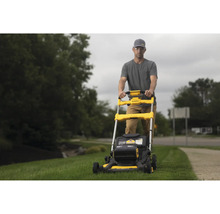 Muž obsluhuje žlutou sekačku na trávu značky DeWalt na zahradě.