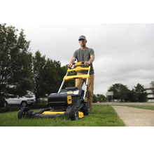 Muž tlačí žlutočernou sekačku na trávu na zahradě.