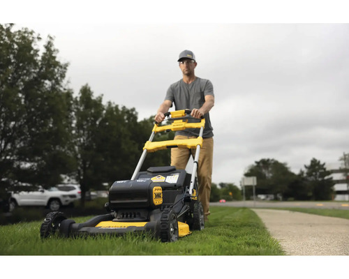 Muž tlačí žlutočernou sekačku na trávu na zahradě.