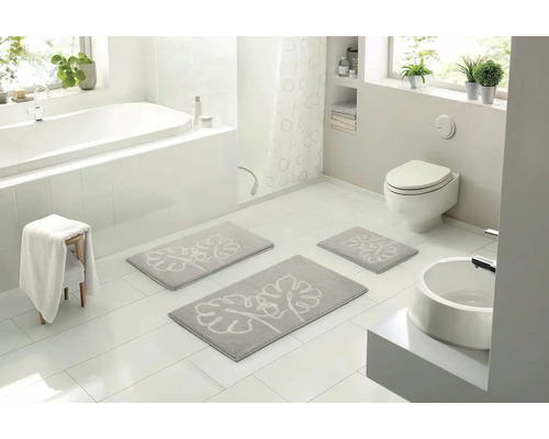 Světlá koupelna s vanou, toaletou a umyvadlem a šedou sadou koupelnových předložek s rostlinným vzorem.