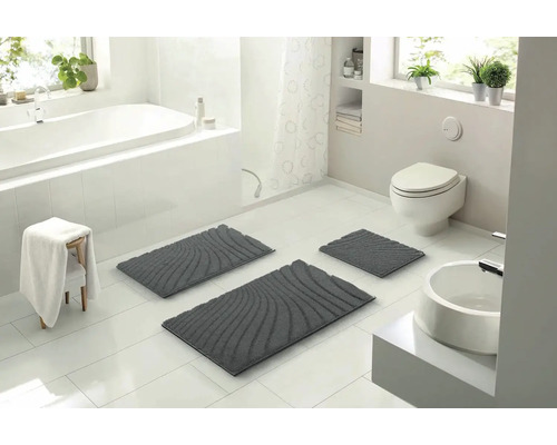 Světlá koupelna s vanou, umyvadlem, toaletou a sadou tří šedých koupelnových koberečků