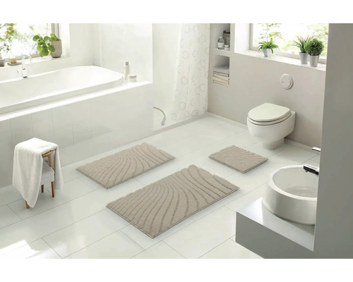 Světlá koupelna s vanou, toaletou, umyvadlem a sadou béžových koupelnových předložek se vzorem vln, skládající se ze tří částí