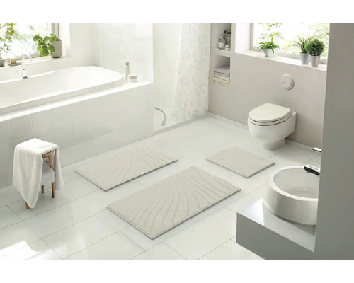 Světlá koupelna s vanou, toaletou, umyvadlem a sadou koupelnových předložek ze tří kusů