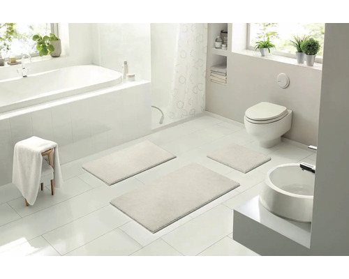 Světlá koupelna s vanou, toaletou, umyvadlem a sadou tří koupelnových předložek