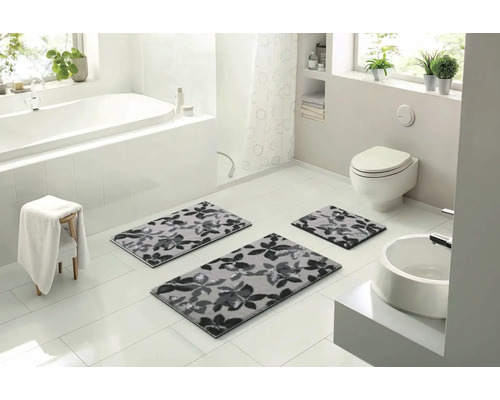 Světlá koupelna s vanou, umyvadlem a třemi šedými koupelnovými předložkami s květinovým vzorem