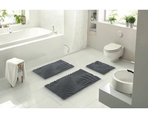 Světlá koupelna s vanou, toaletou a umyvadlem a sada koupelnových koberečků s motivem listů.