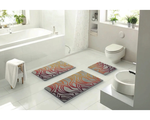 Světlá koupelna s vanou, toaletou, umyvadlem a sadou tří koupelnových předložek se vzorem