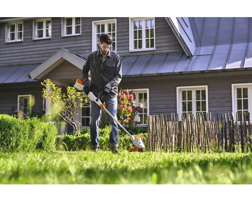 Muž pracuje s akumulátorovým vyžínačem na zahradě před domem.