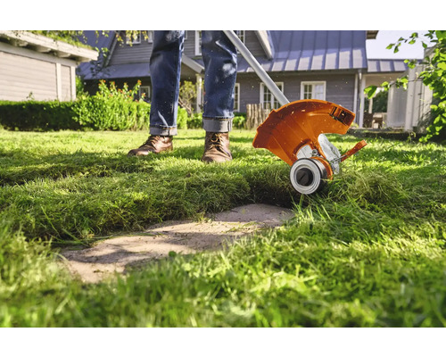 Osoba zastřihuje trávník s vyžínačem v zahradě.