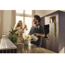 Usmívající se pár zalévá pokojové rostliny konví a rozprašovačem ve světlé místnosti