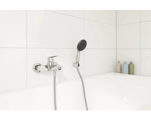 Fotografie vany s baterií a sprchovou hlavicí v koupelně.