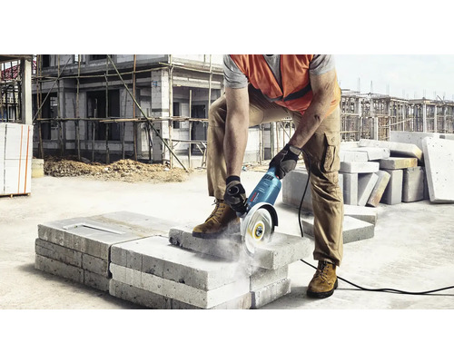 Stavební dělník řeže úhlovou bruskou betonový kámen na staveništi.