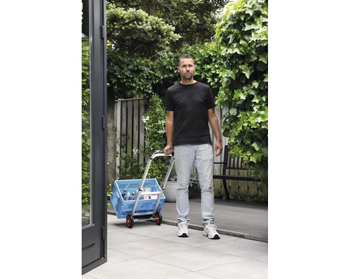 Muž přepravuje modrý nákupní box s vozíkem na zahradě