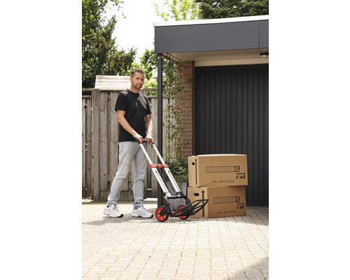 Muž tlačí ruční vozík se dvěma stěhovacími krabicemi před garáží.