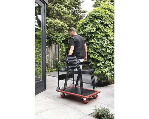 Osoba přepravuje židle v zahradě pomocí skateboardu.