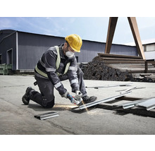 Muž s ochrannou helmou a maskou řeže kov úhlovou bruskou, z níž létají jiskry.