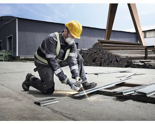 Muž s ochrannou helmou a maskou řeže kov úhlovou bruskou, z níž létají jiskry.