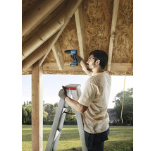 Muž používá akumulátorový šroubovák na žebříku ke stavbě dřevěného domu.