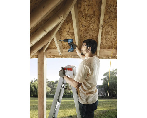 Muž používá akumulátorový šroubovák na žebříku ke stavbě dřevěného domu.