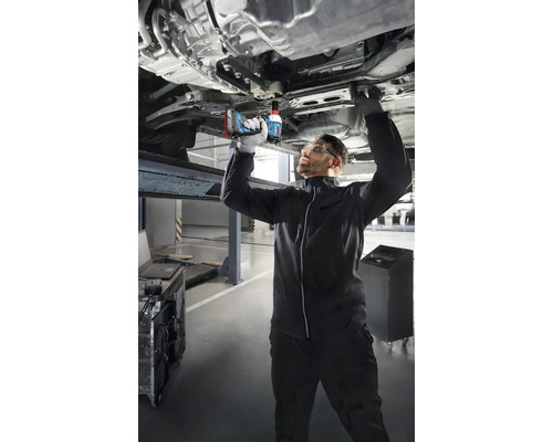 Mechanik používá akumulátorový rázový utahovák k práci na autě, které je na zvedáku.