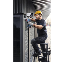 Muž montuje bezpečnostní kameru na budovu pomocí akumulátorového šroubováku.