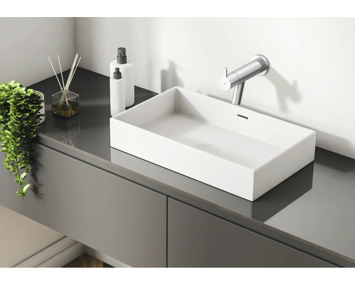 Moderní koupelna s umyvadlem, vodovodní baterií, vonnými tyčinkami a dávkovači pleťové vody na šedé umyvadlové skříňce.