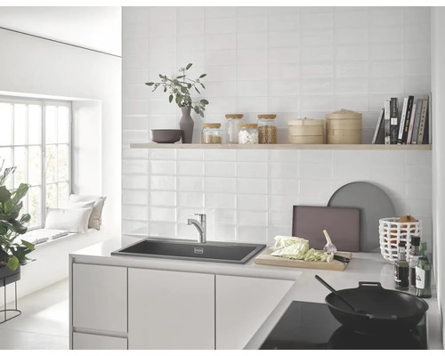 Světlá kuchyně s dřezem, baterií, obklady a kuchyňským náčiním.