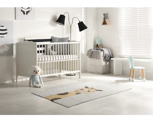 Světlý dětský pokoj s postýlkou, stojací lampou, dětskou židlí a kobercem se zvířecím motivem