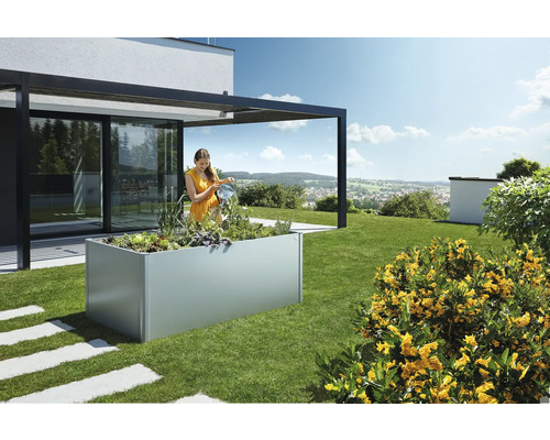 Žena zalévá rostliny ve vyvýšeném zahradním záhonu na zahradě.