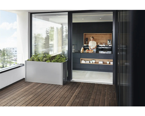 Scéna s truhlíkem na dřevěném balkoně a ženou stojící v kuchyni