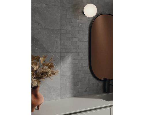 Koupelna s šedými obklady stěn v kamenném vzhledu, zrcadlem a lampou