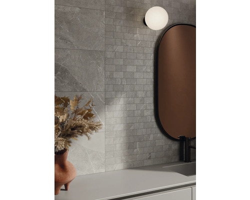 Koupelna s šedými obkladovými dlaždicemi se vzhledem kamene, zrcadlem a lampou