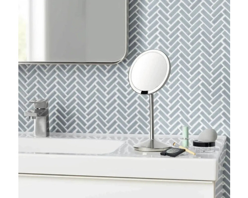 Na umyvadle stojí kulaté kosmetické zrcadlo s podstavcem