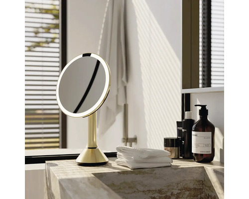 Osvětlené kosmetické zrcadlo v koupelně na mramorovém povrchu s ručníky a produkty péče o pleť.