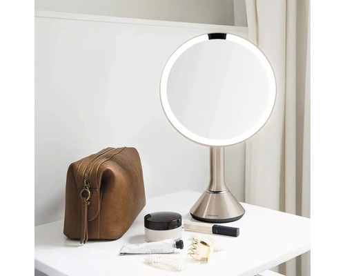 Osvětlené kosmetické zrcadlo s kosmetickou taškou a produkty péče o pleť na stole