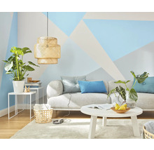 Obývací pokoj s pohovkou, stolem, lampou a pokojovými rostlinami před stěnou s geometrickými vzory