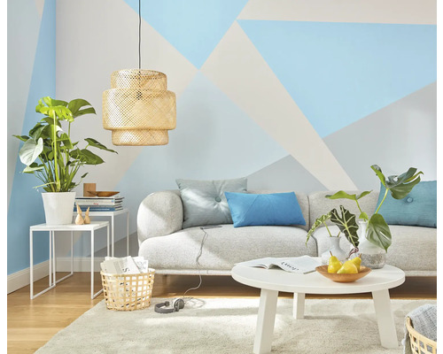 Obývací pokoj s pohovkou, stolem, lampou a pokojovými rostlinami před stěnou s geometrickými vzory