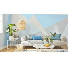 Obývací pokoj s pohovkou, stolem, lampou a pokojovými rostlinami před stěnou s geometrickými vzory