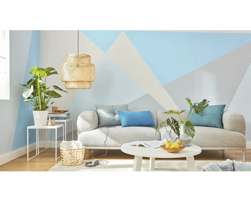 Obývací pokoj s pohovkou, stolem, lampou a pokojovými rostlinami před stěnou s geometrickými vzory