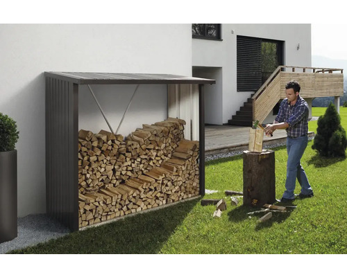 Sklad dřeva s palivovým dřívím a muž štípající dříví na zahradě.