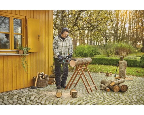 Muž řeže dřevo motorovou pilou na zahradě.