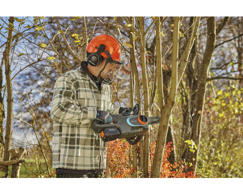 Muž s ochrannou přilbou a akumulátorovou pilou prořezává strom