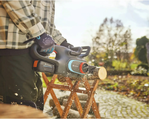 Zahradník řeže akumulátorovou pilou špalek na kozě v zahradě.