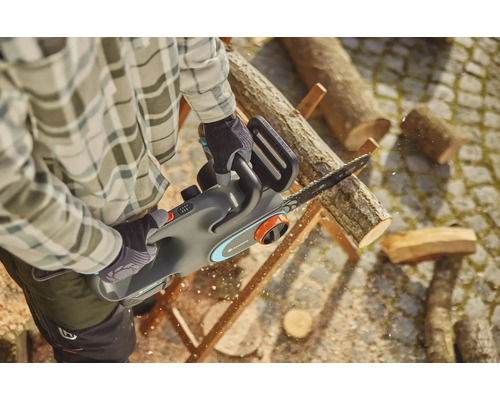 Muž řeže dřevo akumulátorovou pilou Gardena.