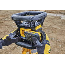 Rotační laser Dewalt s vloženou baterií, ovládaný osobou v pracovních rukavicích.