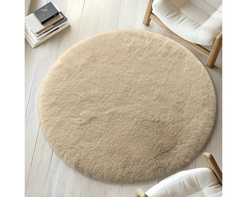 Kulatý béžový koberec na světlé dřevěné podlaze, obklopený židlemi a knihami.