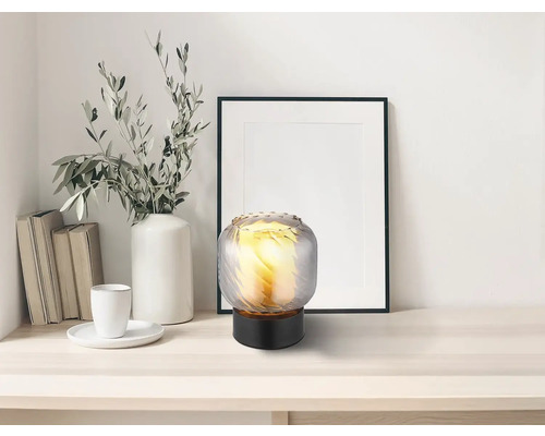 Dekorativní skleněná stolní lampa na stole s dekoracemi, jako jsou knihy, váza s větvemi a zarámovaný obrázek
