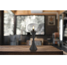 Stolní lampa s průhledným skleněným stínidlem a žárovkou na dřevěném stole